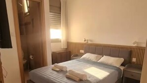 A bedroom with a bed, bedside tables, a window with curtains, and a television on the wall. - AmdarVillage Cozy Garden Apt. (Eilat)