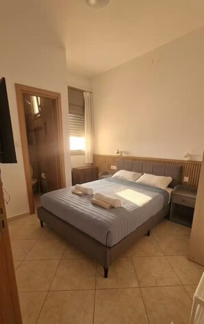 A bedroom with a bed, bedside tables, a window with curtains, and a television on the wall. - AmdarVillage Cozy Garden Apt. (Eilat)