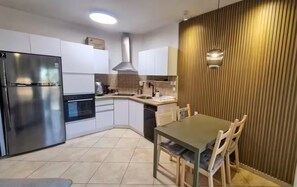 A modern kitchen with a built-in oven, a stainless steel refrigerator, and a dining area with a table and chairs. - AmdarVillage Cozy Garden Apt. (Eilat)