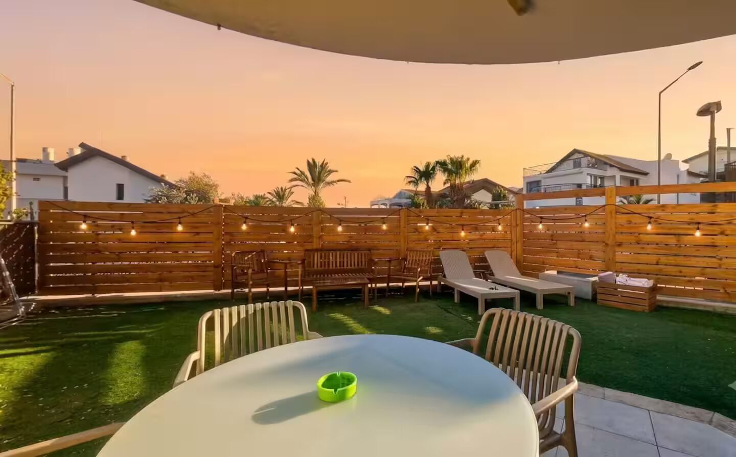 An outdoor patio with a table and chairs, a wooden fence, and a view of the surrounding area.