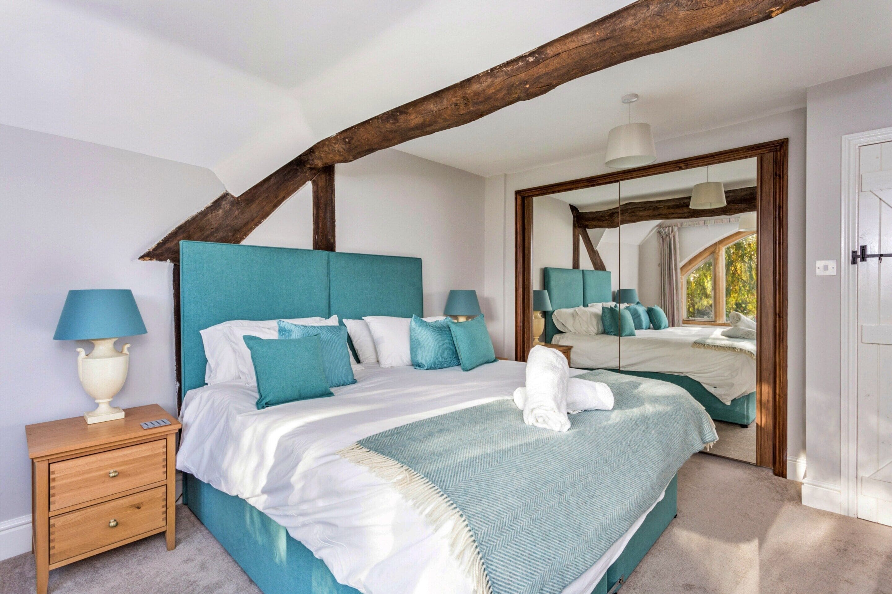 A bedroom with a large bed, two bedside tables, a nightstand, and a mirror.
