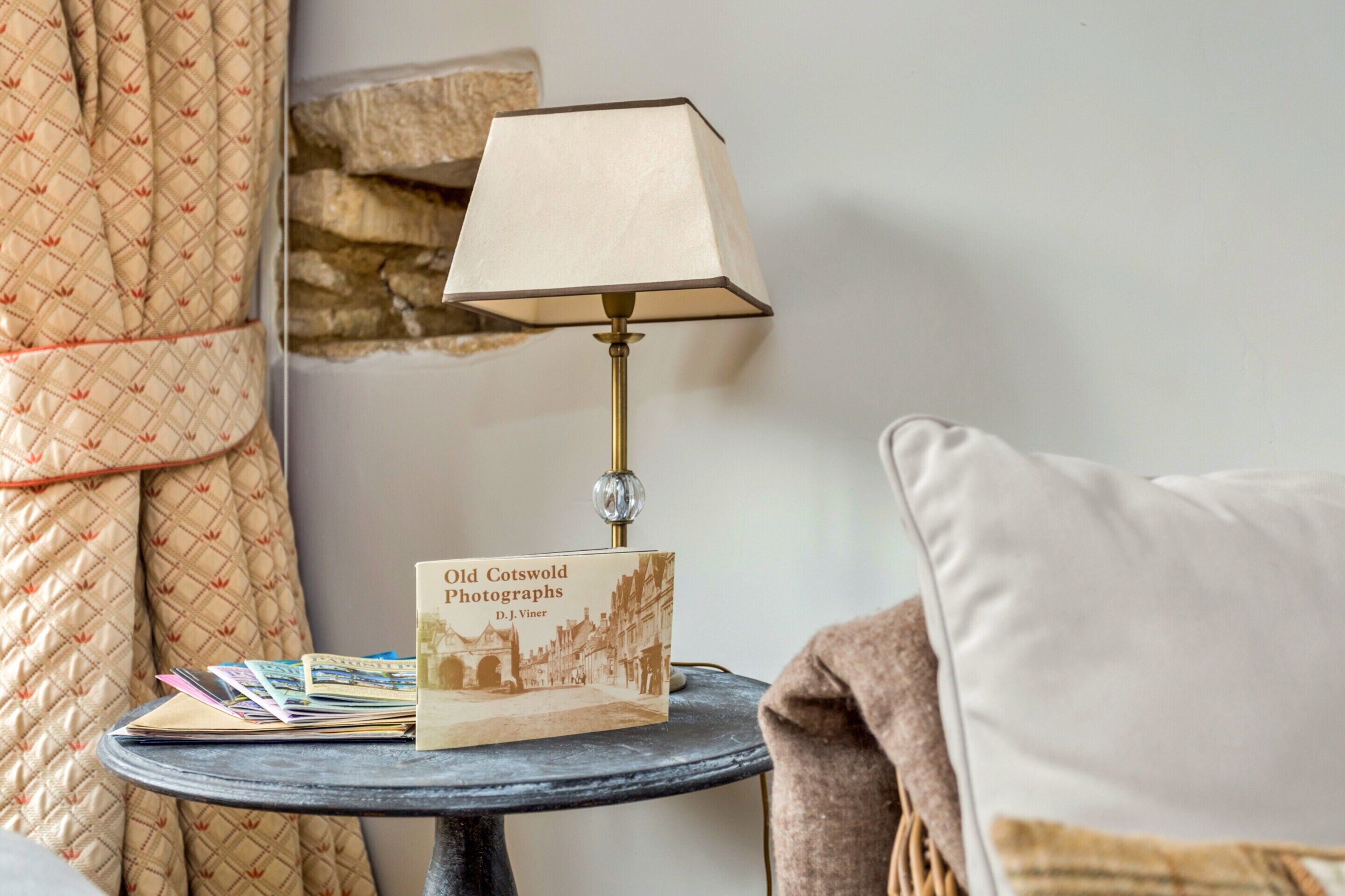 Ein Tisch mit einer Lampe, einem Buch mit dem Titel 'Old Cotswold Photographs' und einigen Zeitschriften.
