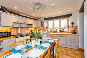 A well-lit kitchen with white cabinets, a dining table set for six, and a large window providing natural light. - Heritage Holiday Barn With Garden (Lechlade)