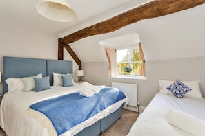 Ein Schlafzimmer mit einem großen Bett, einem kleineren Bett, einem Fenster mit Vorhängen, einer Lampe und einem Balkenbau aus Holz.