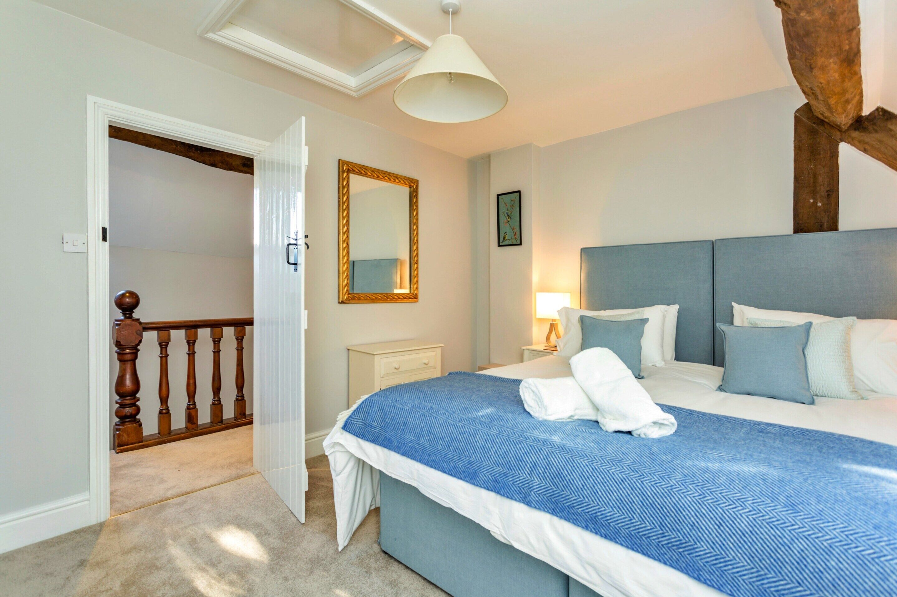 A bedroom with a bed, bedside table, lamp, and a mirror on the wall.