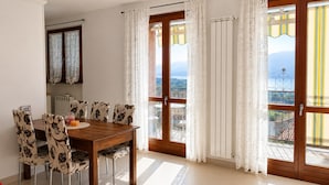 Ein Essbereich mit einem Holztisch, gemusterten Stühlen, einem kleinen runden Tisch und Blick durch ein großes Fenster mit Vorhängen.