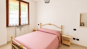 Ein Schlafzimmer mit Bett, Nachttischen, einem Fenster, einer Heizung und einer Hängeleuchte.
