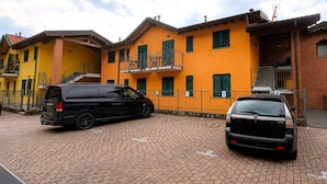 Ein zweistöckiges Gebäude mit gelber Fassade, davor ein schwarzes Auto und ein Pflasterweg.