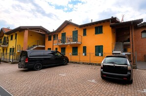 A two-story building with a yellow facade, a black car parked in front, and a brick pathway. - Stunning Pool Apartment With Lake View (Brezzo di Bedero)