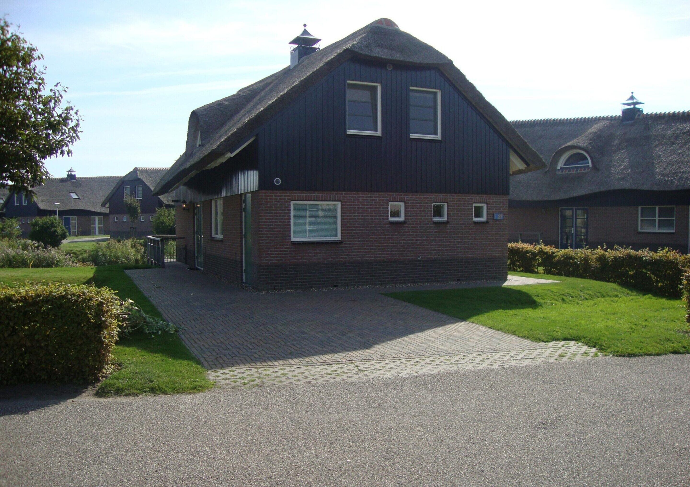 A two-story house with a steeply pitched roof, a brick facade, and a paved driveway.