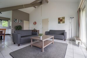 A modern living room with two grey sofas, a wooden coffee table, and a grey rug. There is a small plant on the coffee table and a wall decoration above the door. - Comfortable Bungalow Stay by the Water (Makkum)