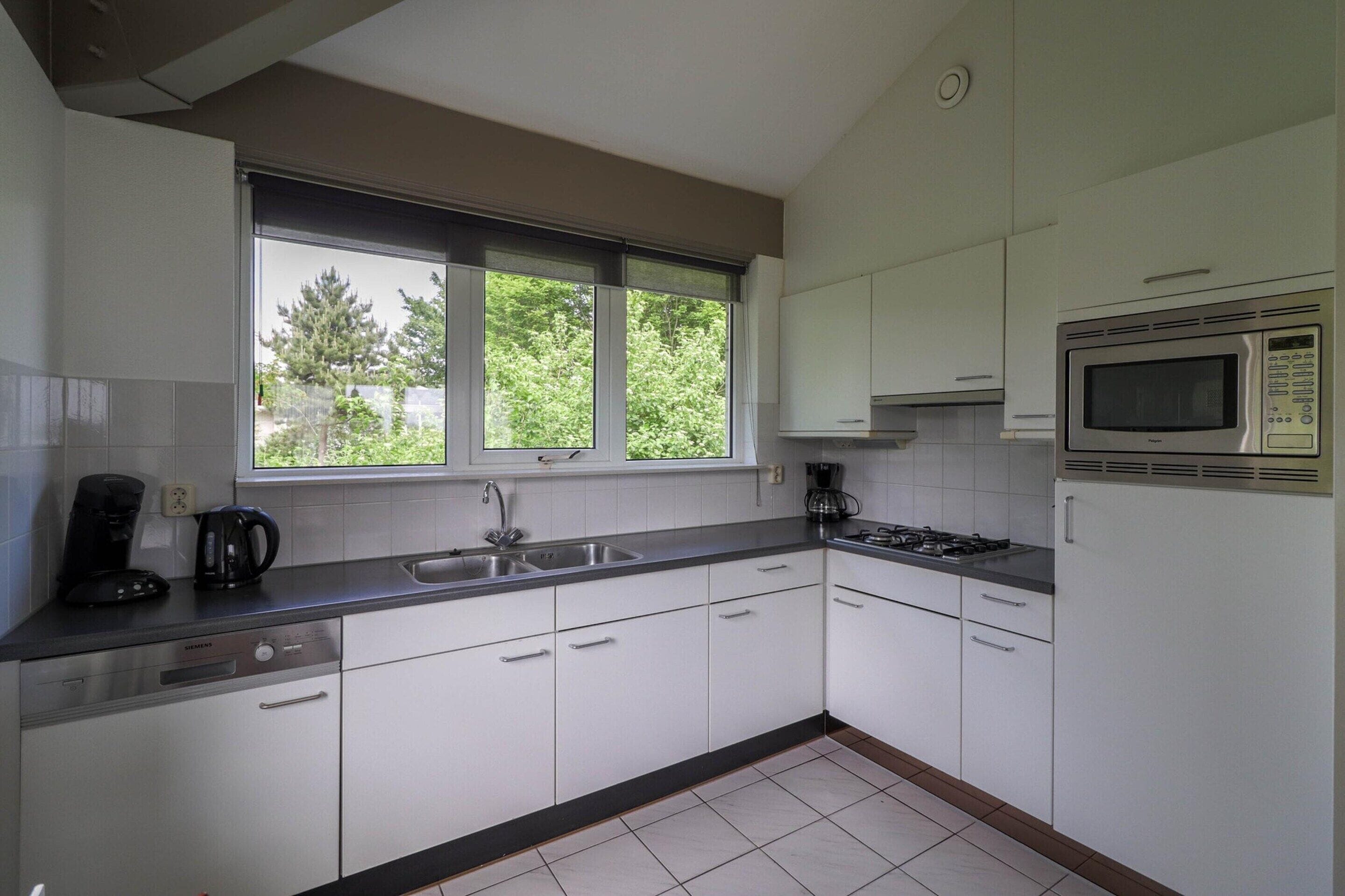 A modern kitchen with white cabinets, a built-in microwave, and a window with a view of greenery.