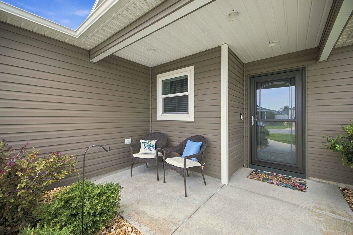 A covered porch with two chairs and a small table, a window, and a door.