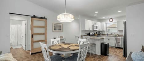 A modern kitchen with white cabinetry, a central island, and a dining area with a round table and chairs.