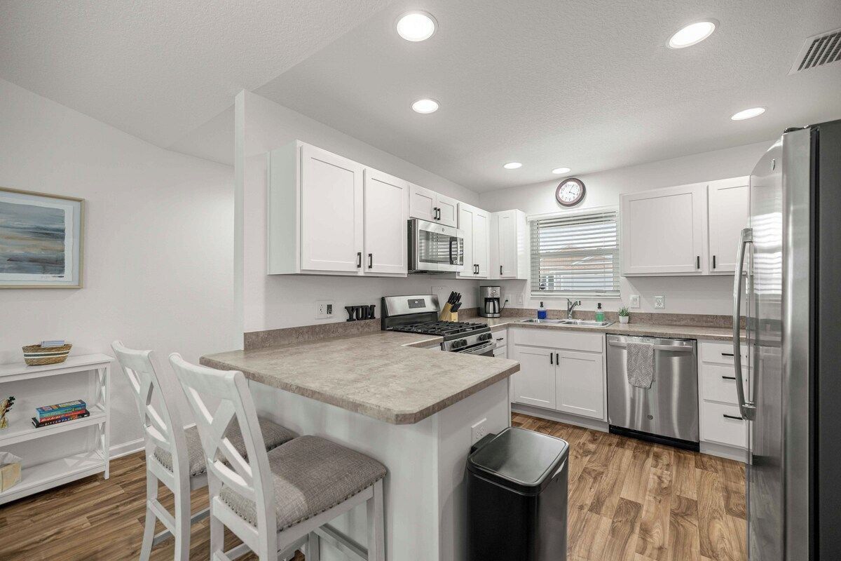 A modern kitchen with white cabinets, a stainless steel refrigerator, and a central island with bar stools.