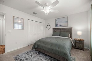 Une chambre à coucher avec un lit, un ventilateur de plafond, une table de chevet avec une lampe et un tableau encadré au mur.