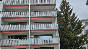 Un edificio residencial de varios pisos con balcones, un garaje y un árbol al fondo.