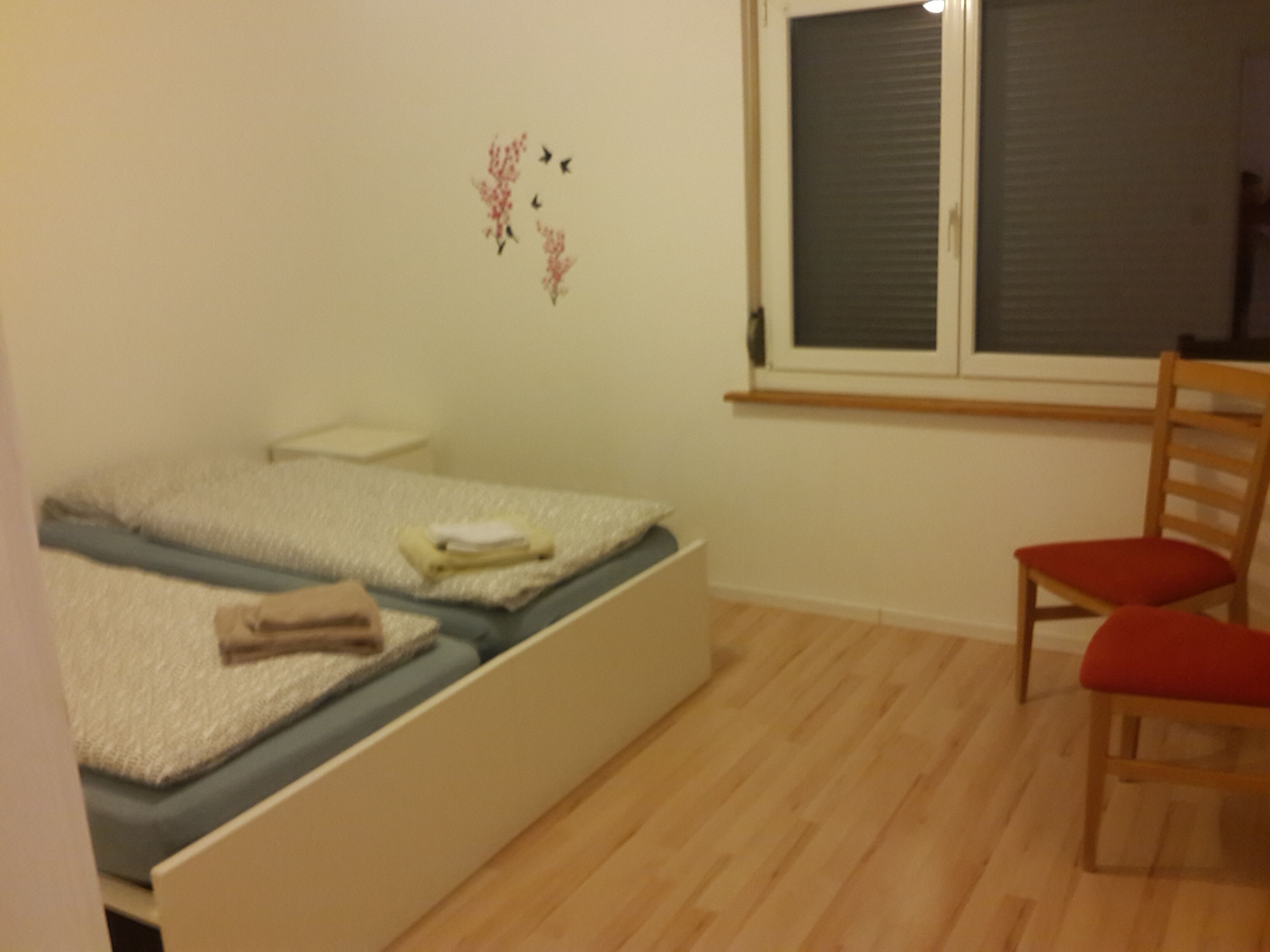 Makuuhuone, jossa on sänky, tuoli, ikkuna ja seinäkoriste.