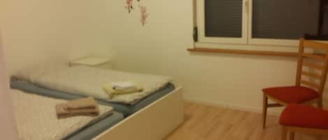 A bedroom with a bed, a chair, a window, and a wall decoration.