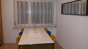 A room with a white table, yellow chairs, a window with sheer curtains, and a framed picture on the wall.