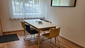 Un comedor con una mesa y sillas, una ventana con cortinas y un espejo montado en la pared.