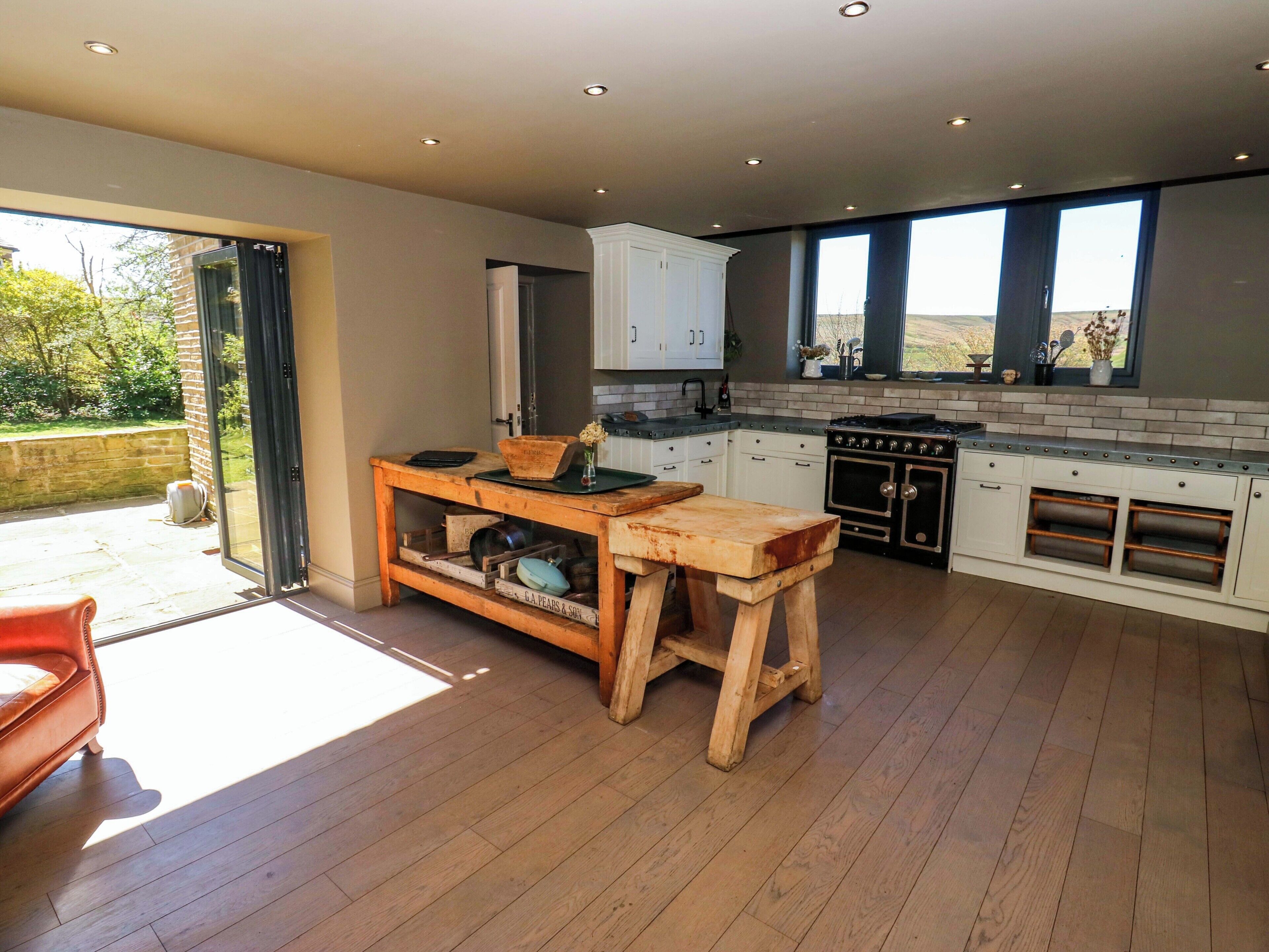 A modern kitchen with wooden flooring, a central island, and a view through large windows.