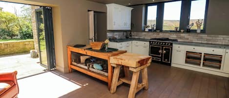 A modern kitchen with wooden flooring, a central island, and a view through large windows.