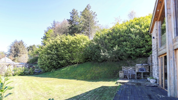 Une terrasse en bois mène à un bâtiment en pierre doté d’une cheminée et d’un espace salon extérieur.
