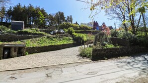 Un chemin pavé qui monte une pente, avec un mur de pierres d’un côté et une zone herbeuse avec des arbres de l’autre.