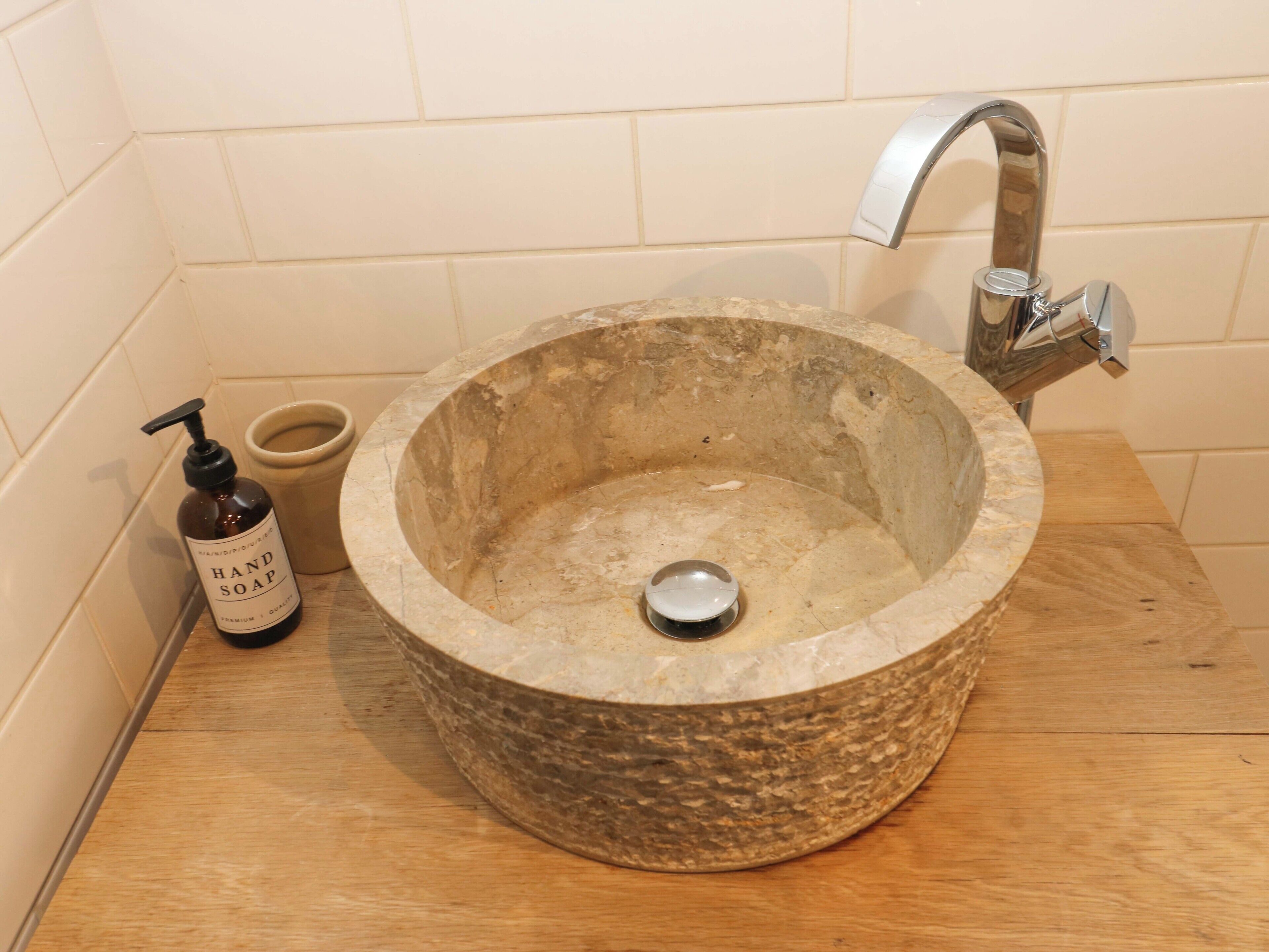 A stone sink with a faucet, a soap dispenser, and a small cup on a wooden countertop.