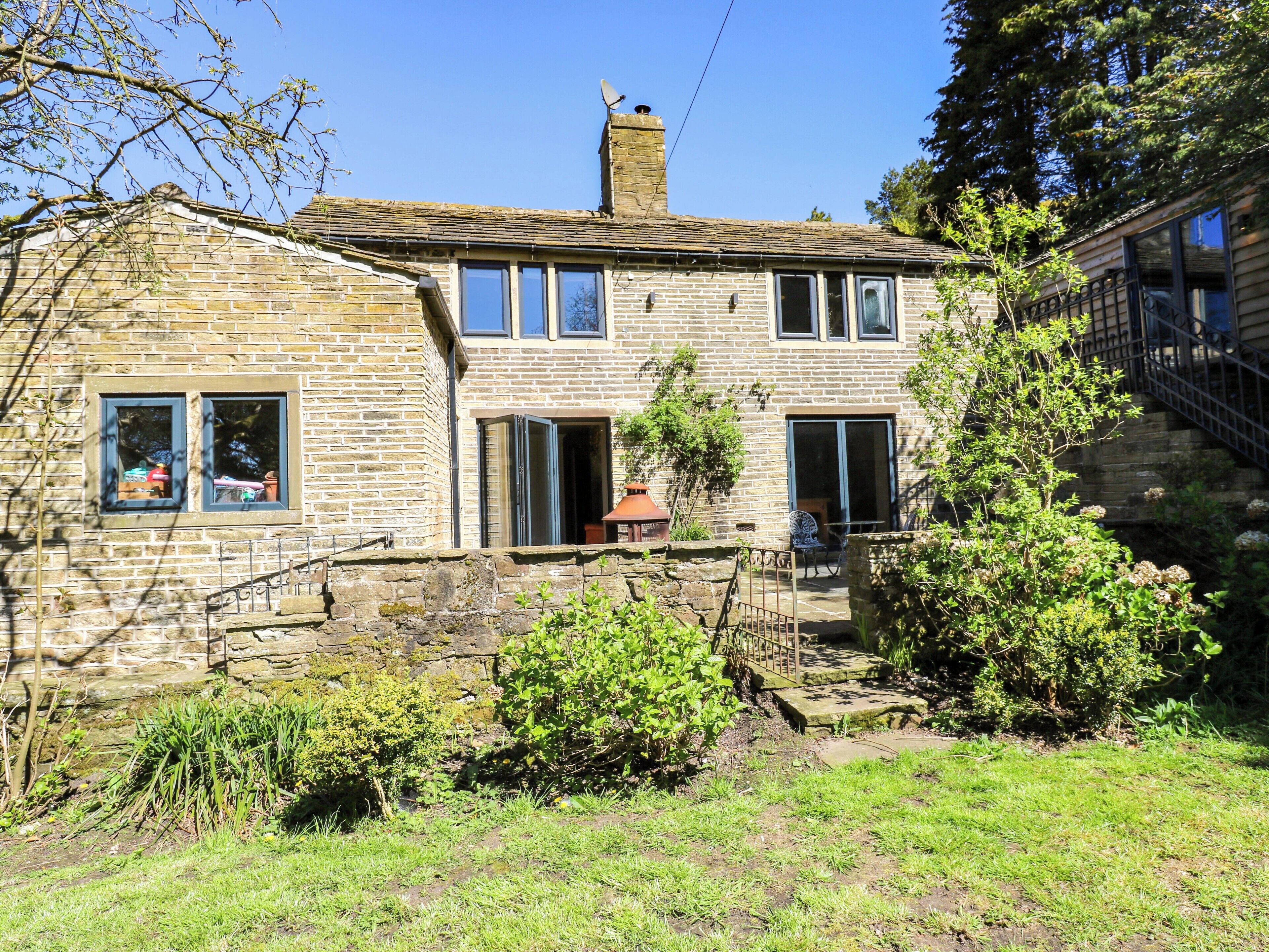 A stone house with a chimney, a small garden, and a staircase leading to a deck.