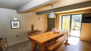 Un coin repas avec une table et un banc en bois, un luminaire suspendu et une vue sur l’extérieur grâce à une porte vitrée.