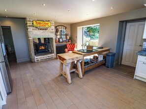 A rustic kitchen with a stone wall, a wooden table, a fireplace, and a window with a view of greenery. - Rocks Cottage (Halifax)