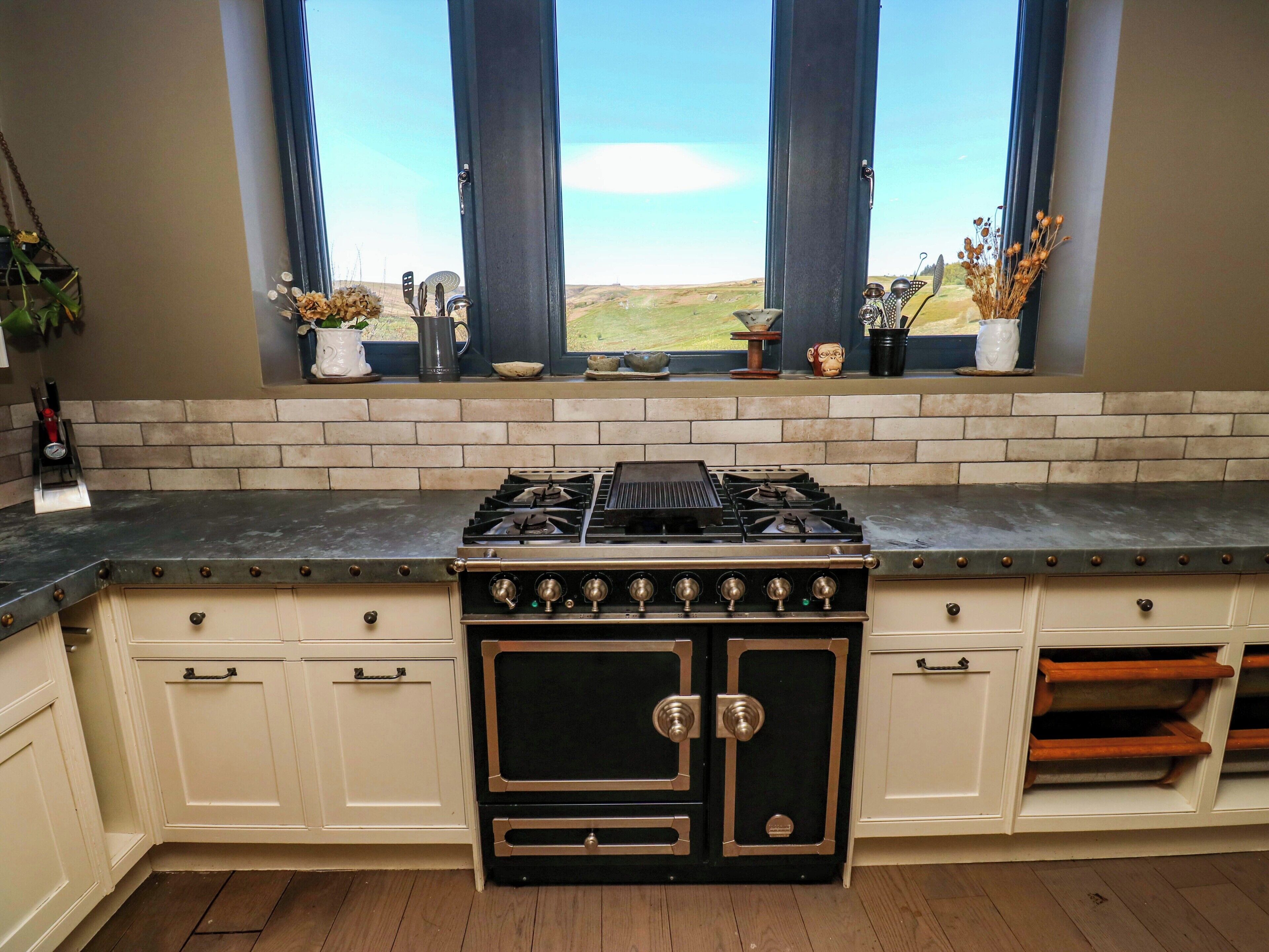 Una cocina con estufa a gas, armarios blancos y ventana con vistas.