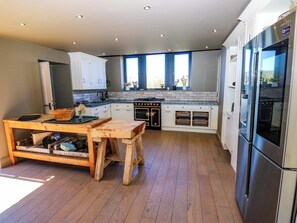 Eine moderne Küche mit weißen Schränken, einem Holztisch, einem Edelstahlkühlschrank und einem eingebauten Ofen.