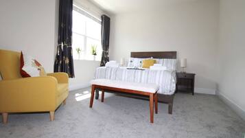 A bedroom with a bed, a bench, a nightstand, a lamp, and a window with curtains.