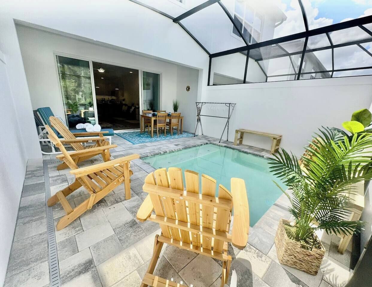 A pool area with wooden chairs, a table, and a glass-enclosed space.