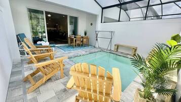 A pool area with wooden chairs, a table, and a glass-enclosed space.