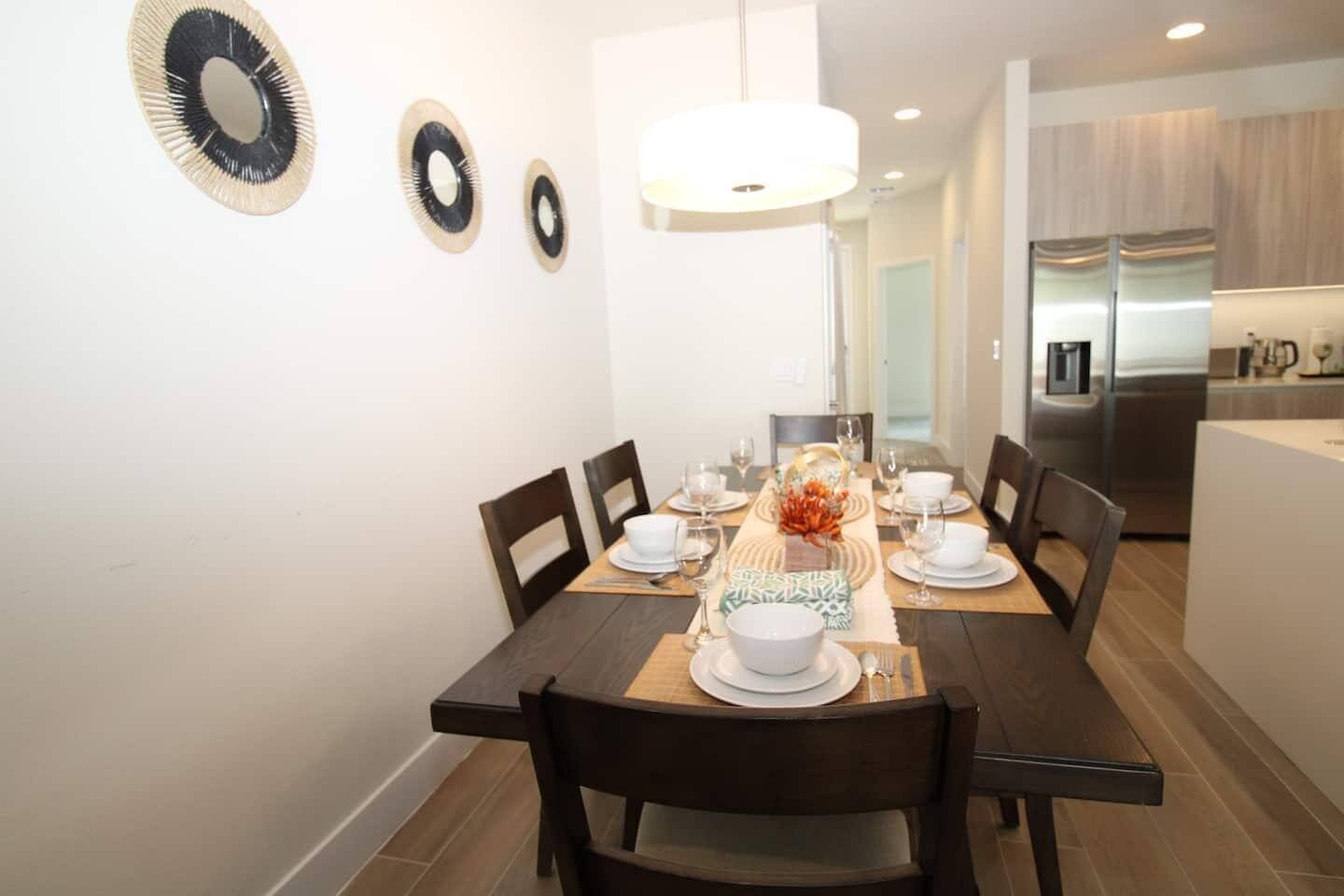 Un comedor con una mesa de madera dispuesta para cuatro personas, sillas y una lámpara colgante moderna.
