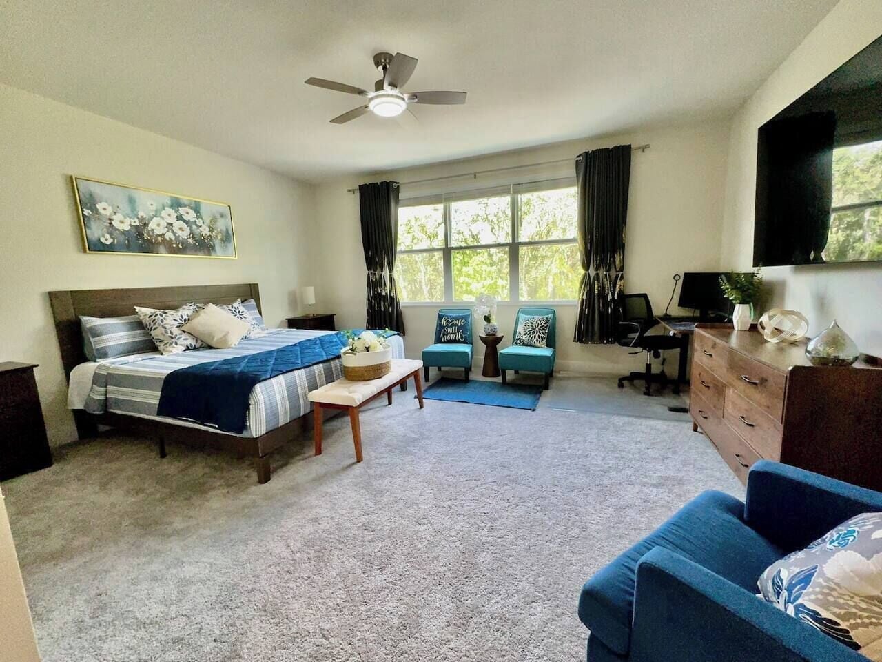A bedroom with a bed, a desk, a chair, a dresser, and a window with curtains.