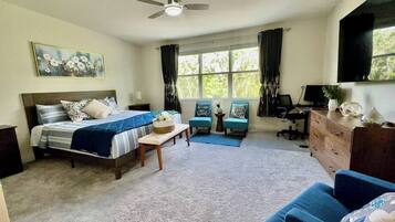 A bedroom with a bed, a desk, a chair, a dresser, and a window with curtains.
