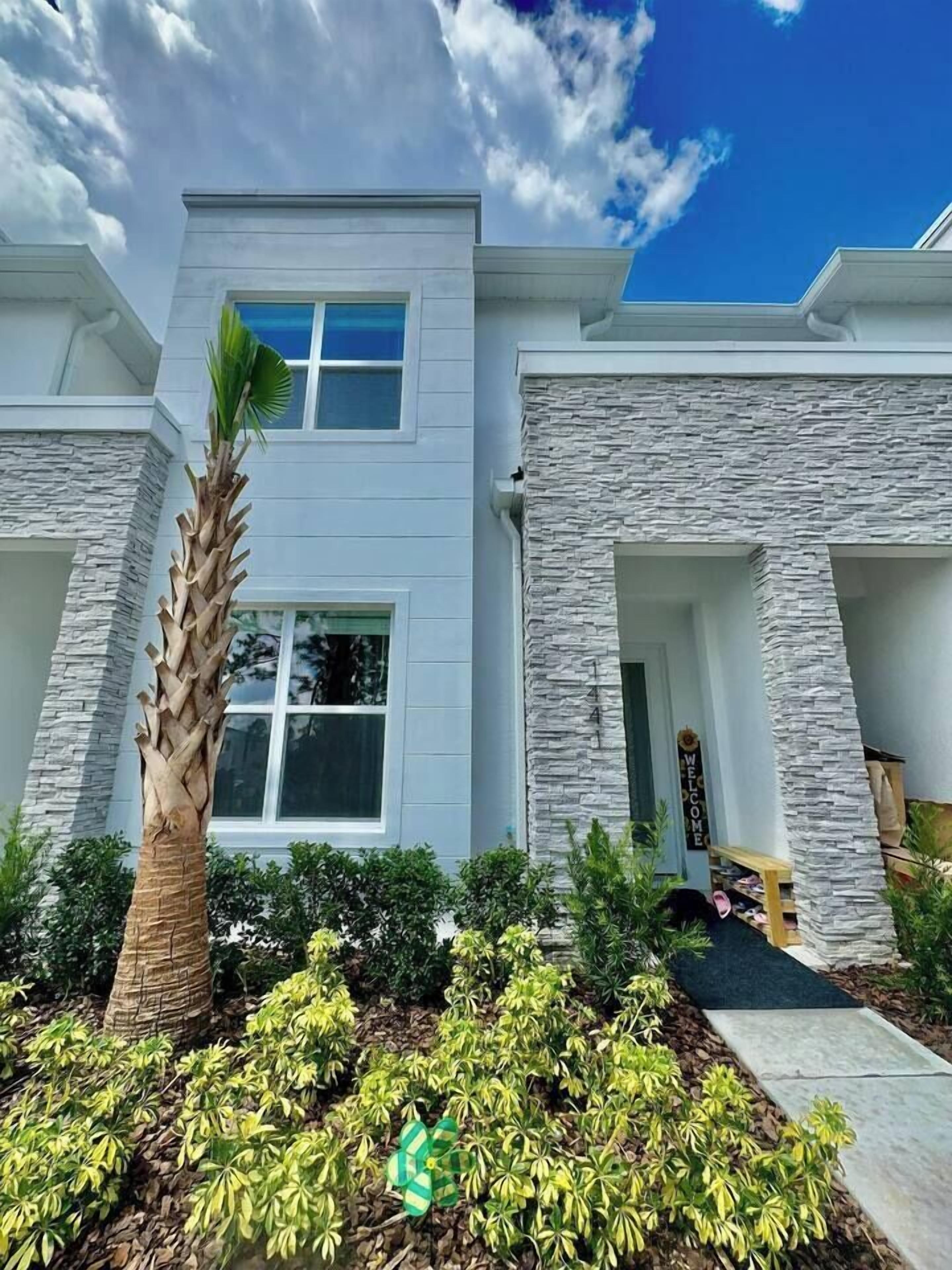 A modern two-story house with a stone facade, a palm tree, and a well-maintained garden.