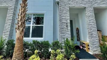 A modern two-story house with a stone facade, a palm tree, and a well-maintained garden.