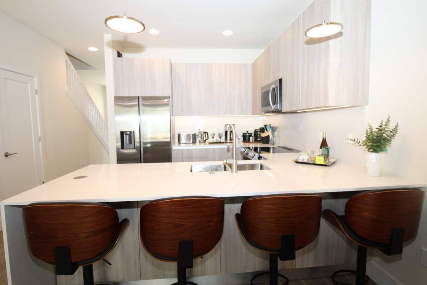 A modern kitchen with a large island, stainless steel appliances, and wooden bar stools.