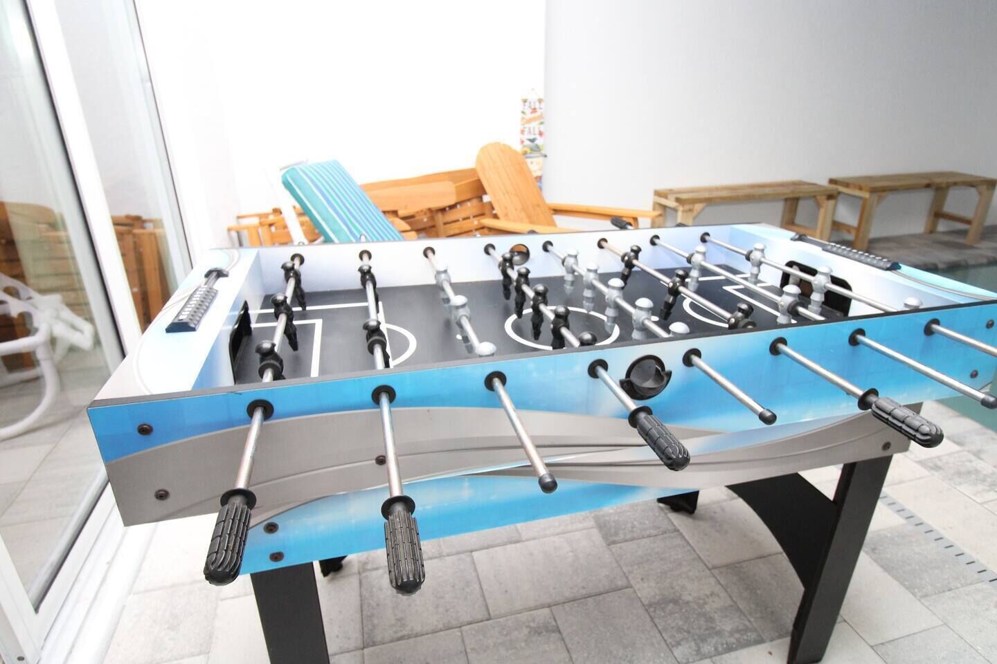 A foosball table in a room with a glass wall, wooden furniture, and a tiled floor.