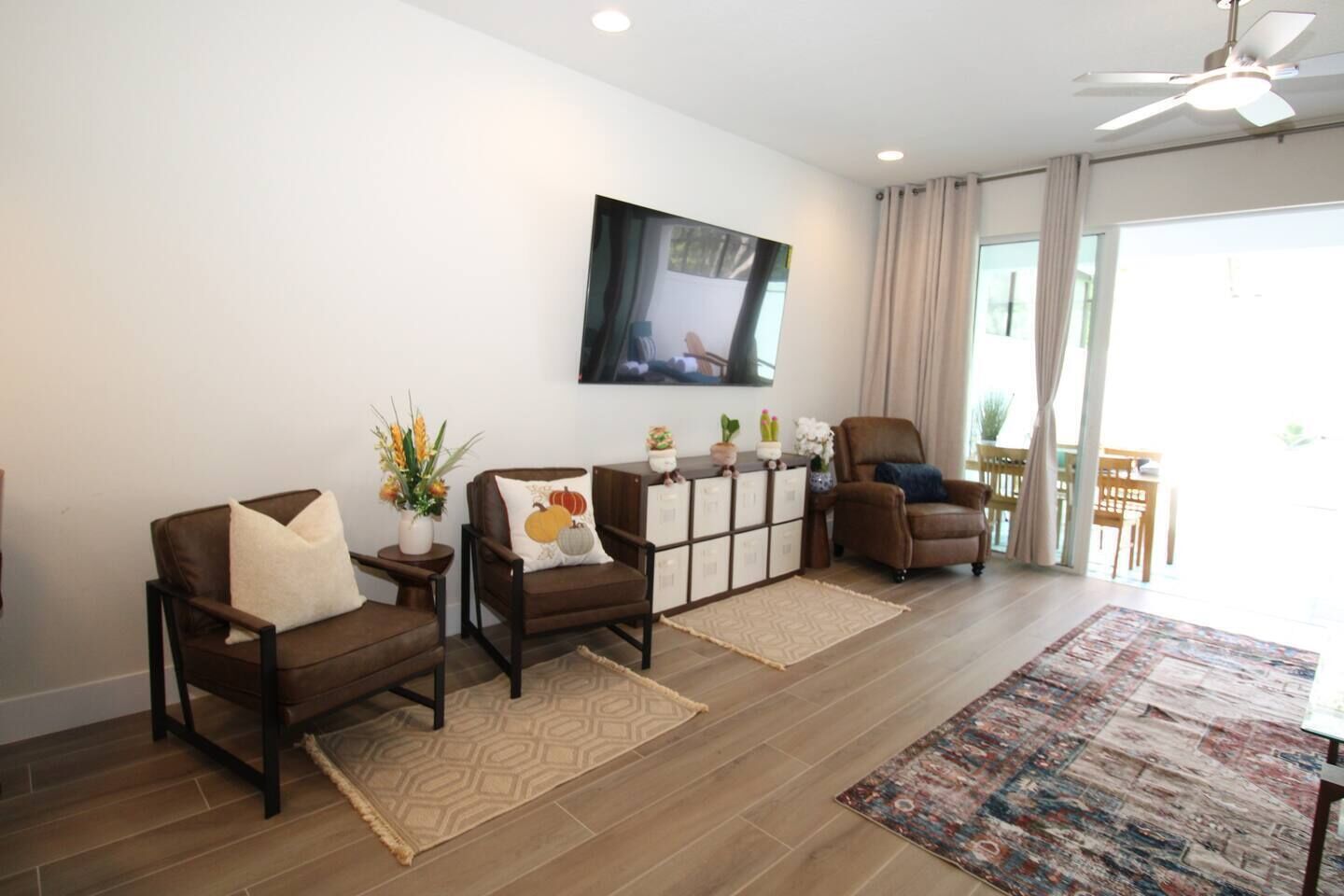 A modern living room with two brown leather chairs, a coffee table, a TV mounted on the wall, and a view of the outdoors through large windows.