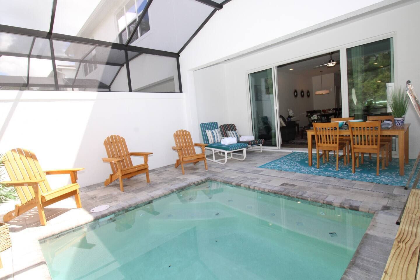 A pool area with wooden chairs, a table, and a glass door leading to a room.