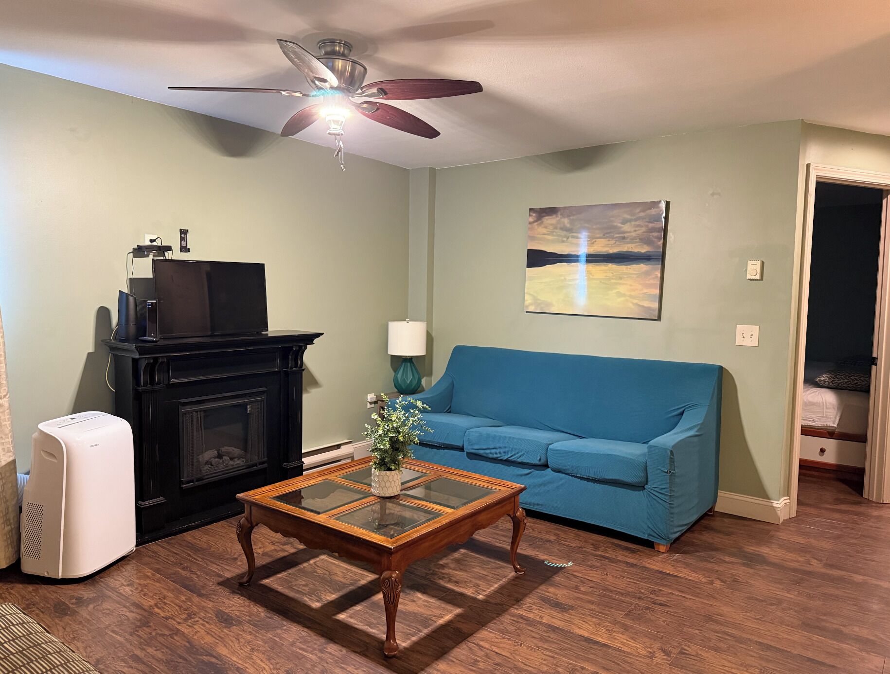 A living room with a fireplace, a blue sofa, a coffee table with a plant, and a ceiling fan.