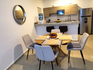 A modern kitchen with a dining area, including a round table with chairs, a microwave, and a refrigerator. - Dream 2-bedroom apartment in Puerto Morelos with pools, gym, tennis court & more (Puerto Morelos)