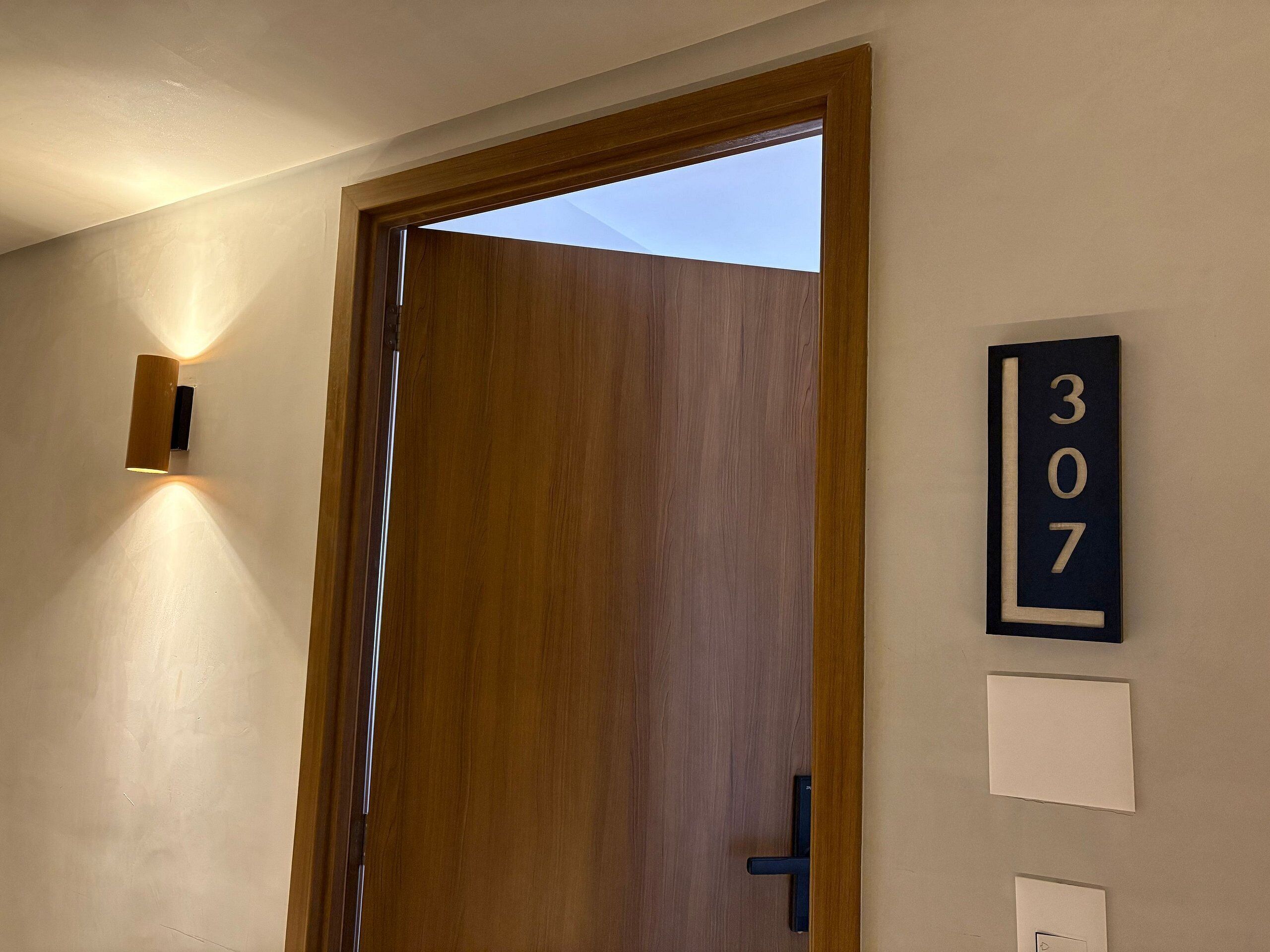 A wooden door with a number plaque indicating room 307, a wall-mounted light, and a door handle.